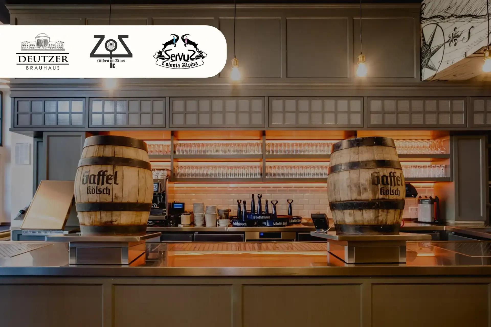 Two wooden Gaffel Kölsch beer barrels prominently displayed on a sleek bar counter with glasses.